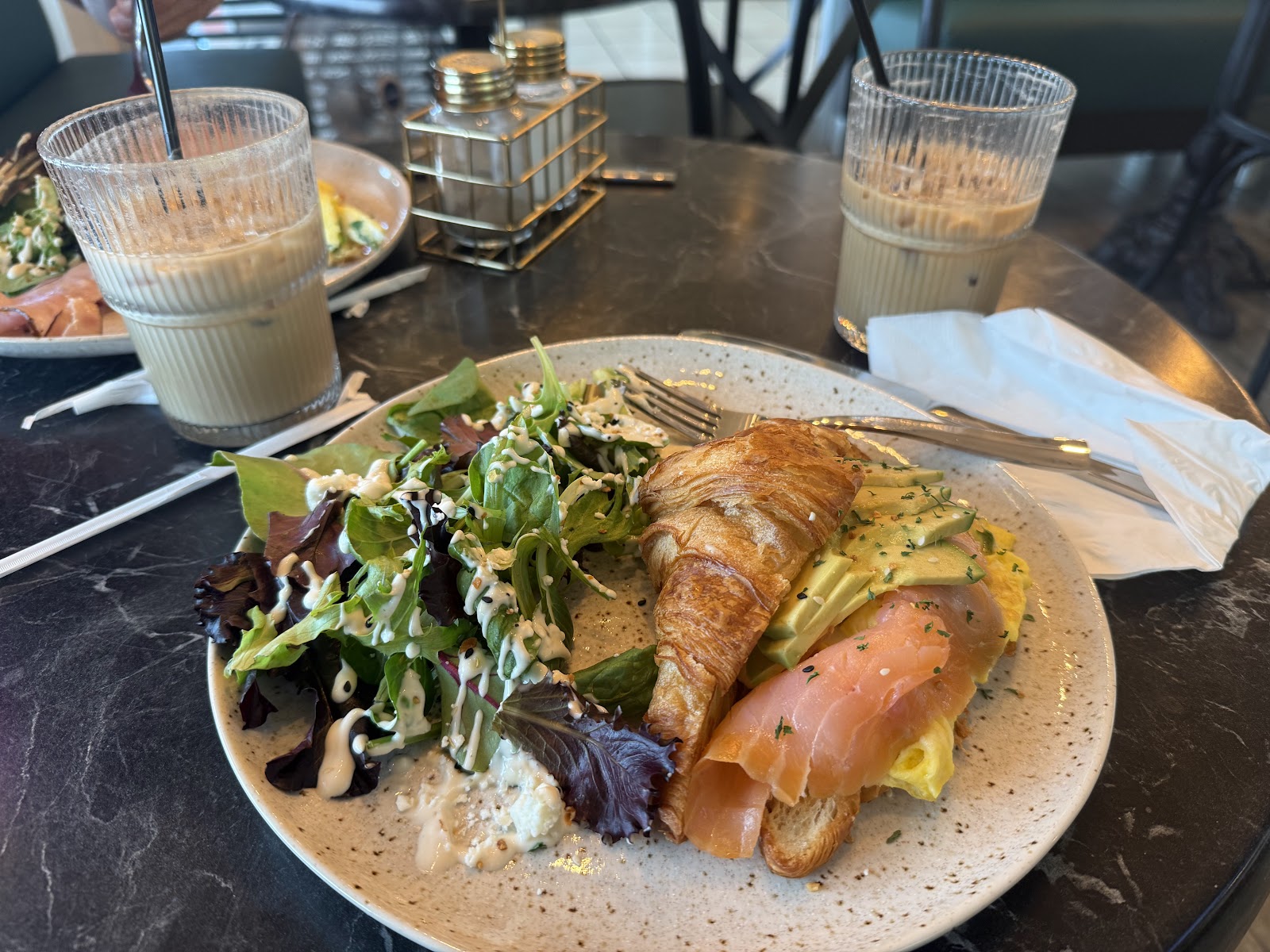 A breakfast plate with a filled croissant, egg and a side of greens