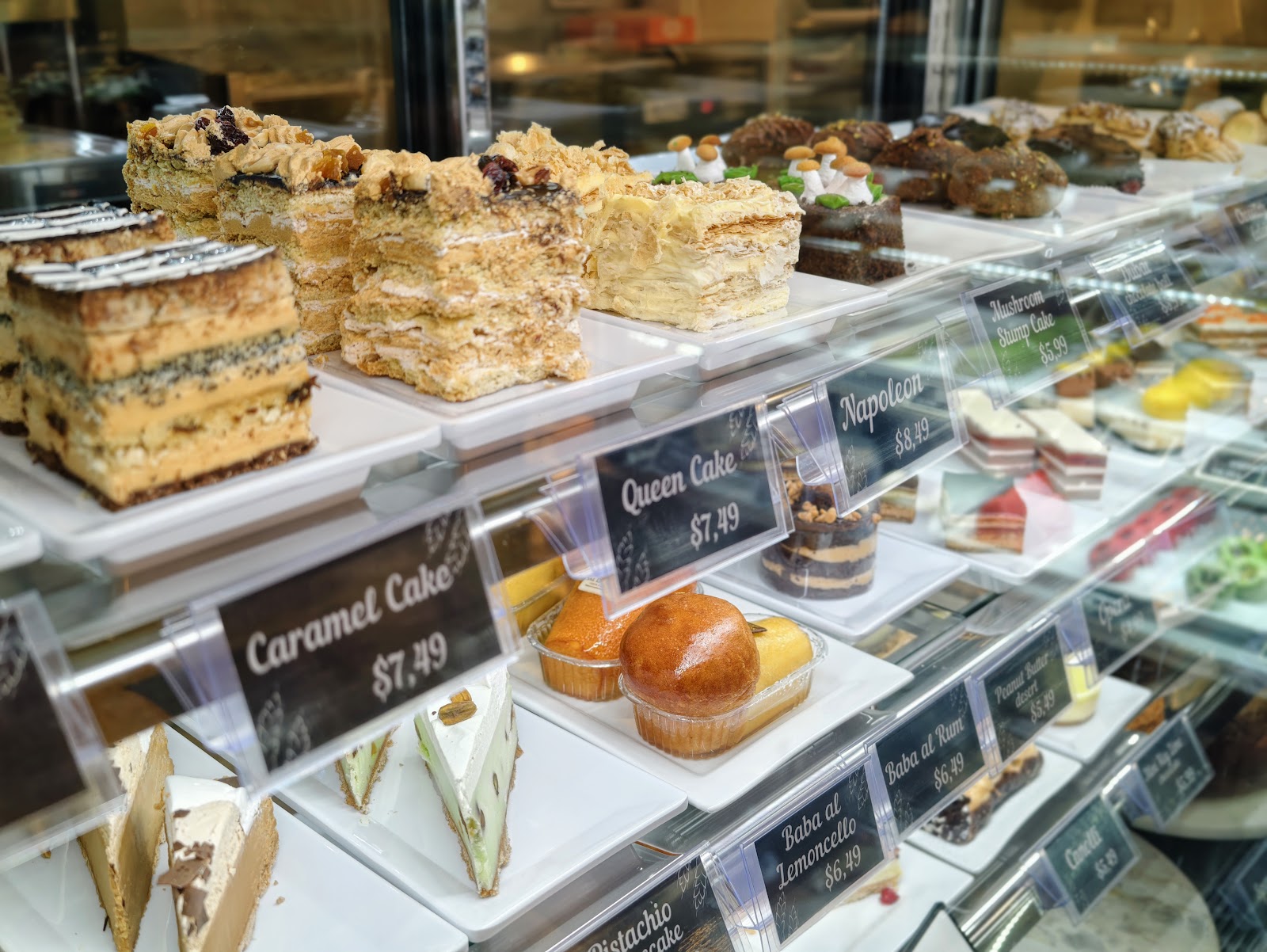 A refrigerated case of layered cakes and pastries with name cards