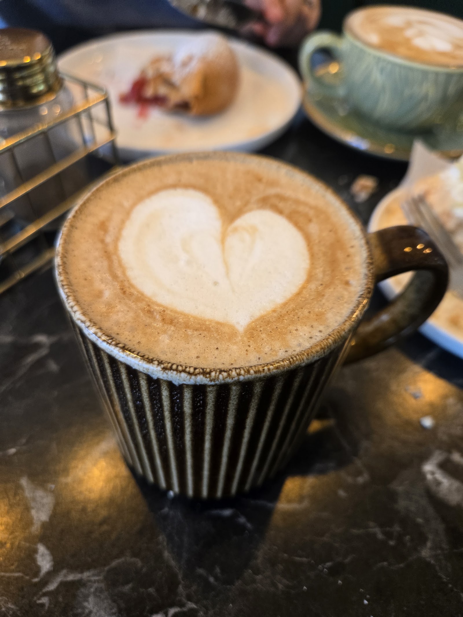 A cappuccino with heart latte art in a striped cup on a dark marble table