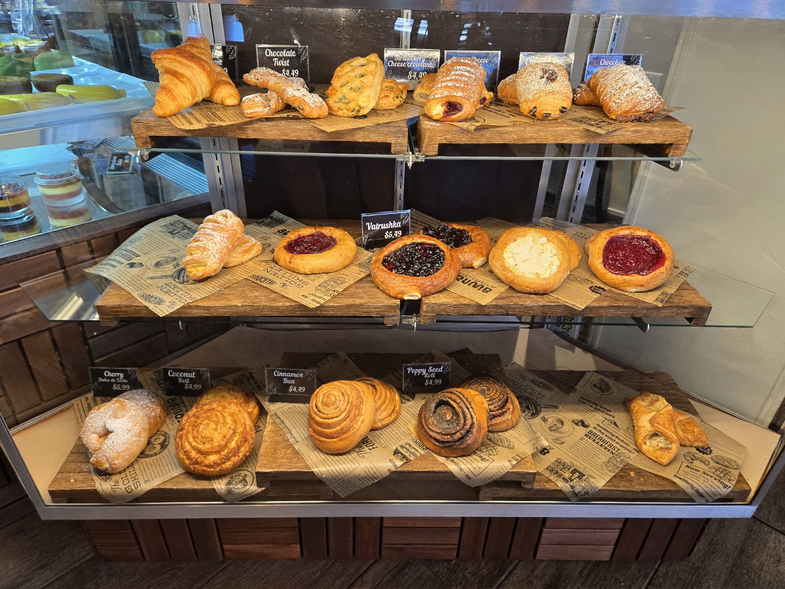 A wooden display of croissants, danishes and cinnamon rolls with handwritten labels